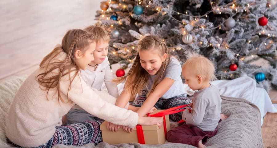 Children opening a gift near a Christmas tree.